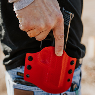 An image of a man reaching for his firearm safely secured on his OWB (Outside the Waistband) Holster.