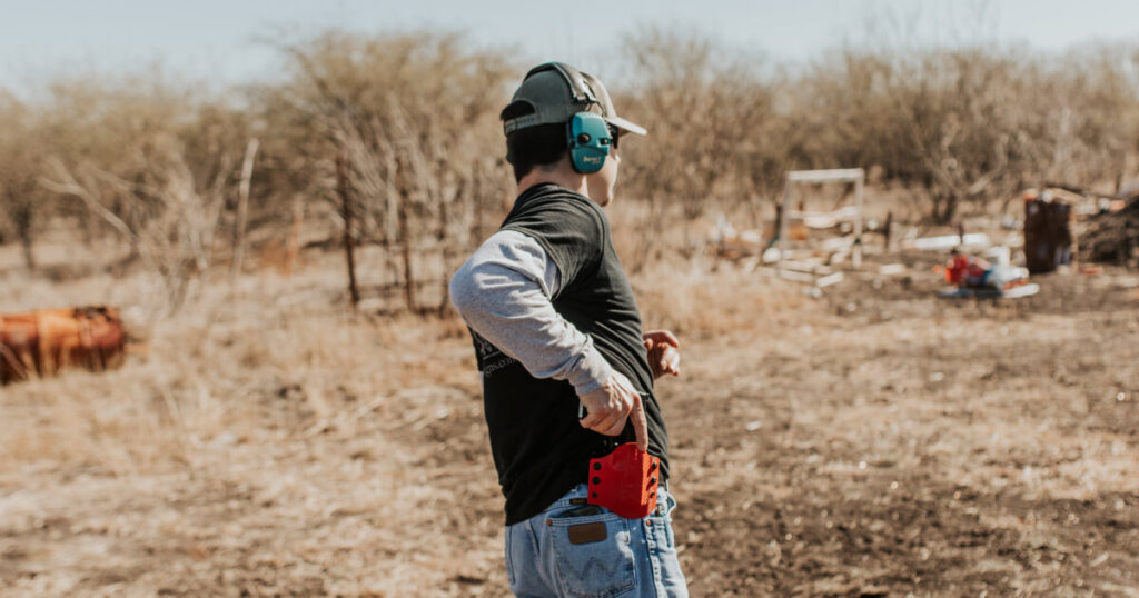 An image of a man reaching for his firearm safely secured on his OWB Holster (Outside the Waistband) at a shooting range during firearms training.